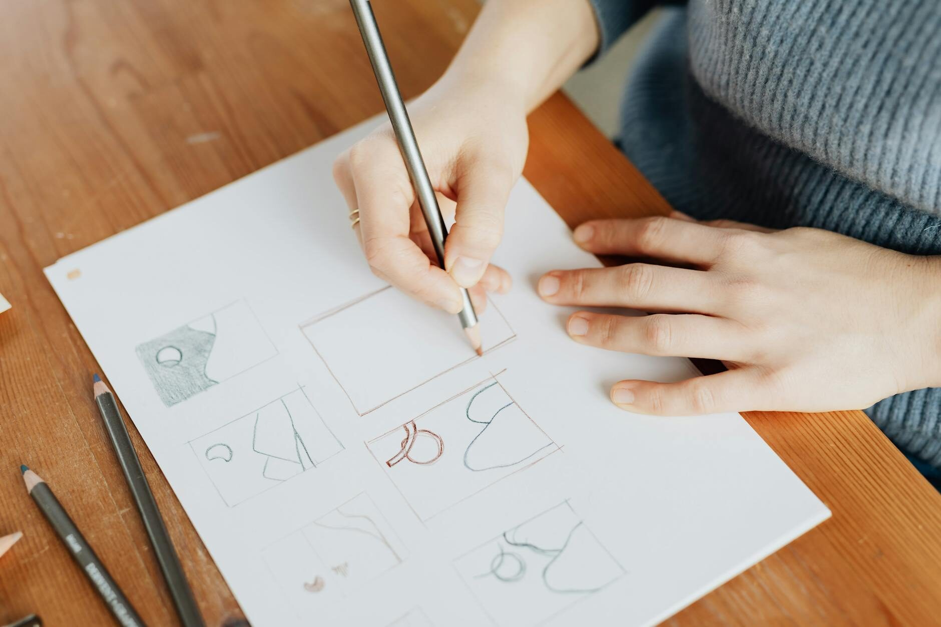 Hands sketching logo concepts on white paper with pencils on a warm wood table
