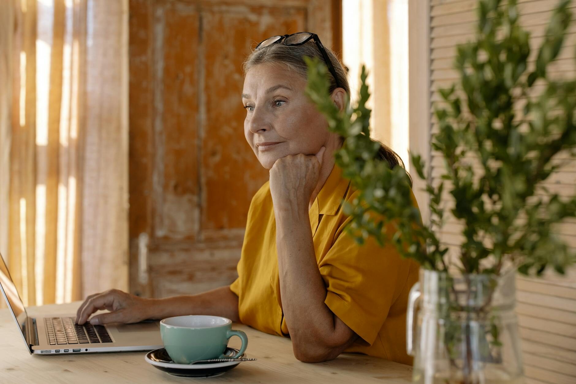 Creative professional at her desk with laptop and coffee in a warm natural-light workspace